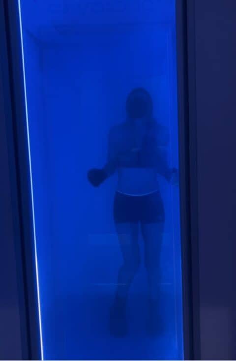 a female inside a whole body cryotherapy chamber surrounded by blue light