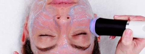 A female is having a facial using a handheld wand (Geneo), she has blue oxygenating product on her face