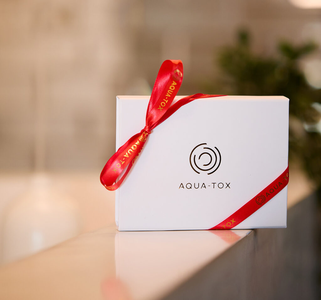 A small white box embossed with a gold Aqua Tox logo and tied with Aqua Tox red ribbon