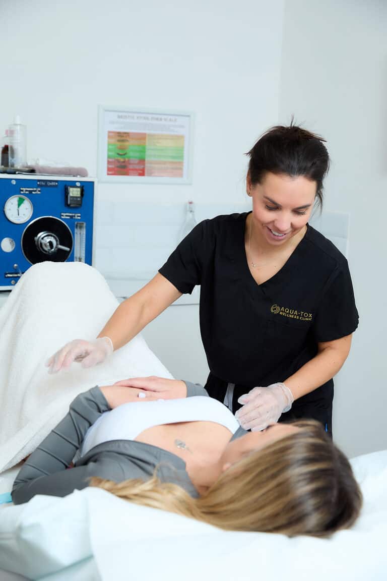 a female therapist talks to a patient on a treatment bed during a colonic irrigation treatment