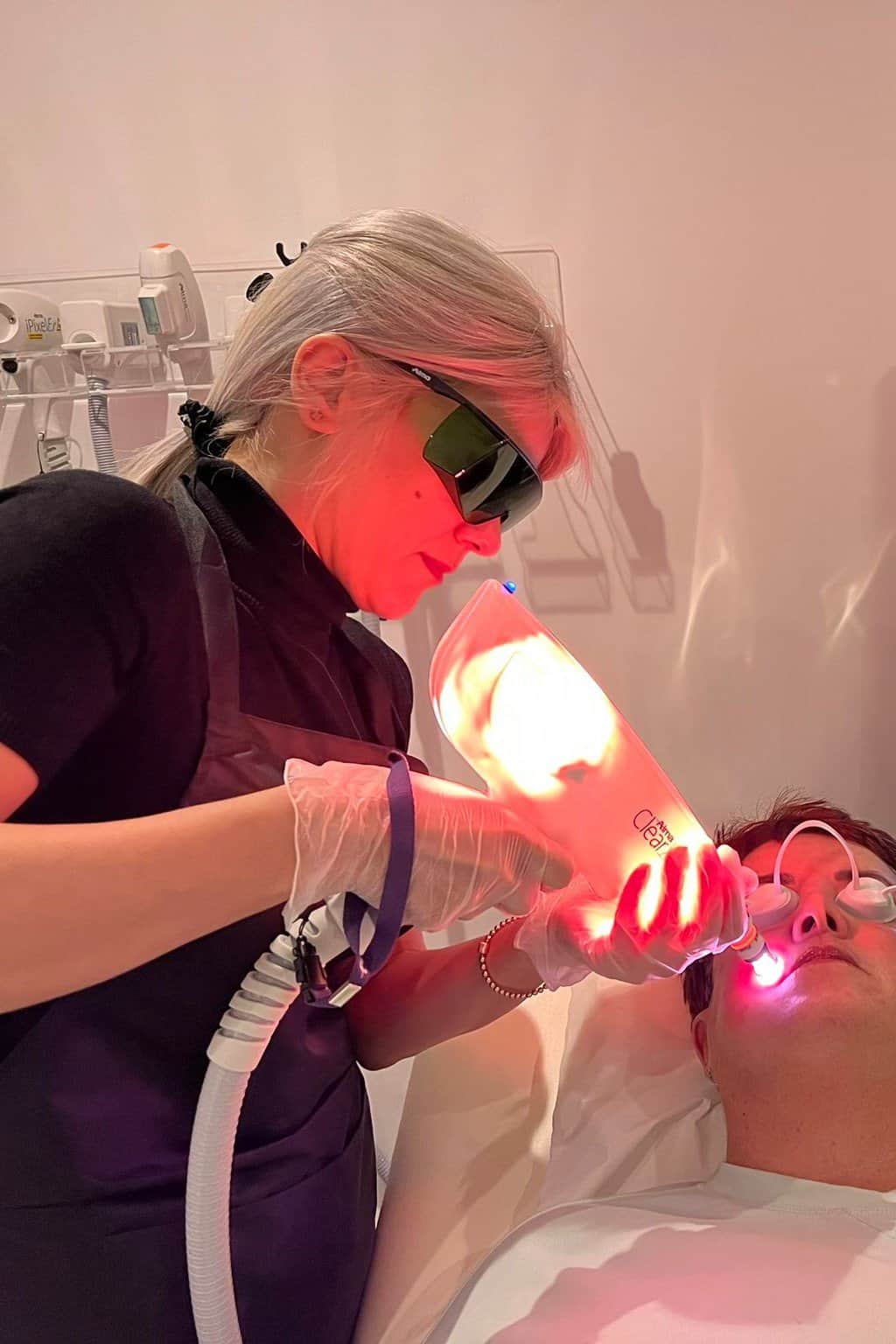 A female therapist is holding a facial laser and performing a treatment on a female clients face