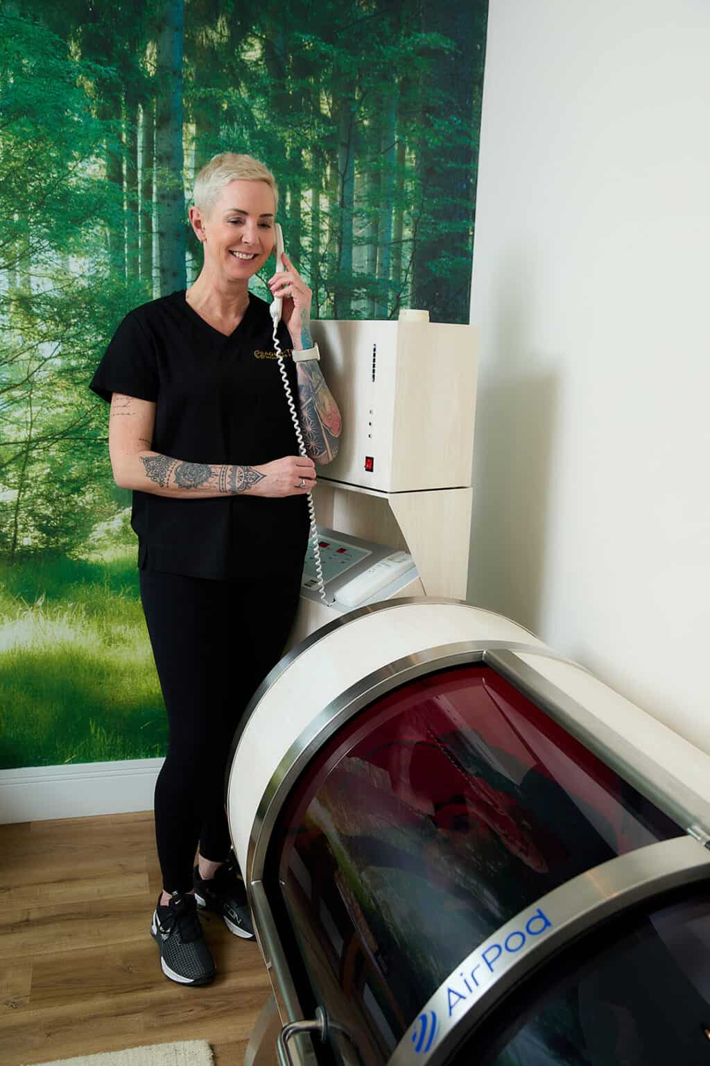 a female with short platinum blonde hair speaks to a client in a hyperbaric oxygen chamber through a telephone intercom system