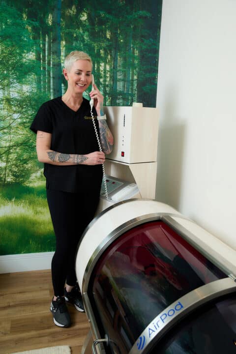 a female with short platinum blonde hair speaks to a client in a hyperbaric oxygen chamber through a telephone intercom system